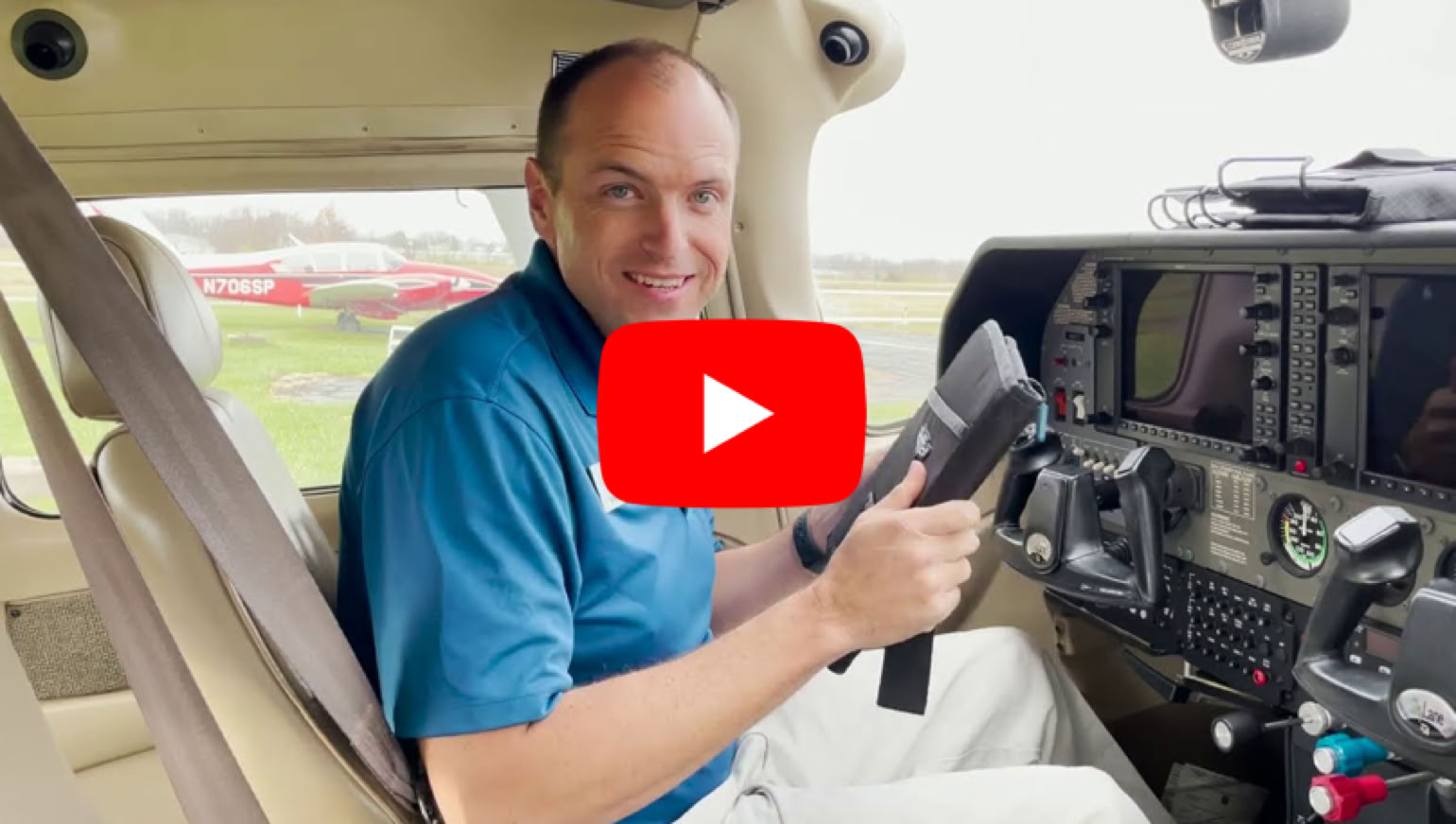 Man in een vliegtuigcockpit met een blauwe polo, zittend op de stoel en kijkend naar de camera.