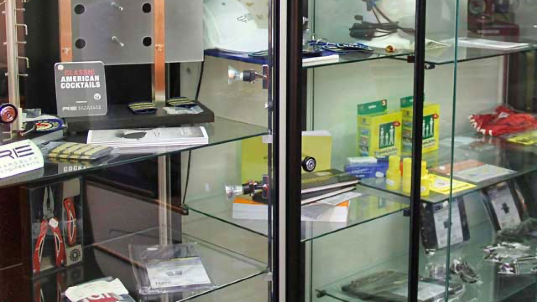 Glazen vitrinekast met diverse elektronische apparaten voor vliegtuigen en accessoires, waaronder kabels, verpakkingen en folders.